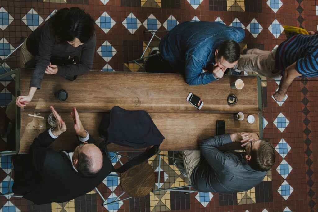 Vijf werknemers van bovenaf gefotografeerd aan een tafel in gesprek met elkaar